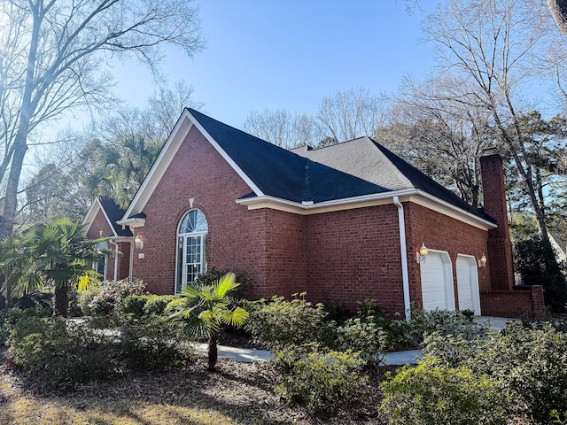 view of side of property with brick siding, an attached garage, a chimney, and a shingled roof