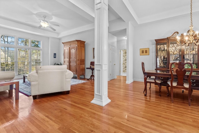 living area with light wood-style floors, a raised ceiling, and ornate columns