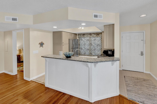 kitchen with light wood-type flooring, freestanding refrigerator, visible vents, and light stone countertops