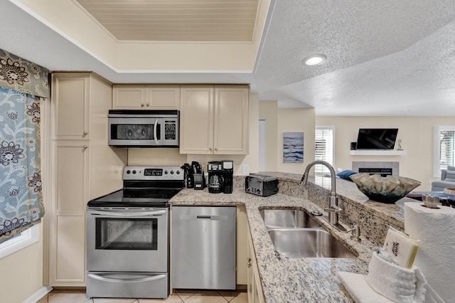 kitchen featuring cream cabinets, stainless steel appliances, a sink, a wealth of natural light, and a raised ceiling