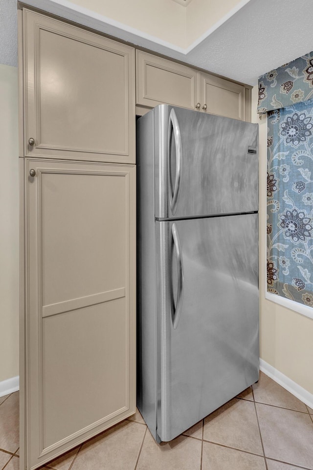 kitchen with light tile patterned floors, baseboards, light countertops, cream cabinetry, and freestanding refrigerator