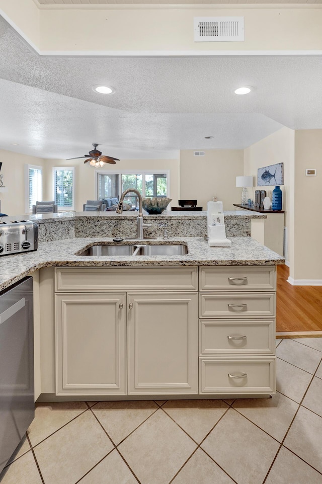 kitchen featuring dishwasher, a sink, visible vents, and light stone countertops