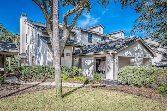 townhome / multi-family property with a front yard, roof with shingles, a chimney, and stucco siding