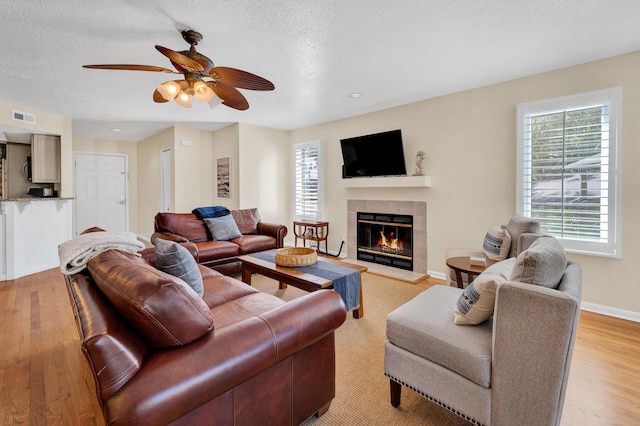 living area with light wood finished floors, visible vents, a tiled fireplace, a textured ceiling, and baseboards