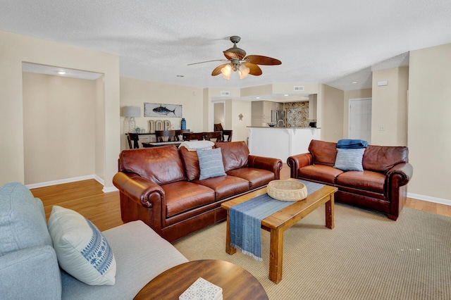 living room featuring a textured ceiling, a ceiling fan, light wood-style flooring, and baseboards