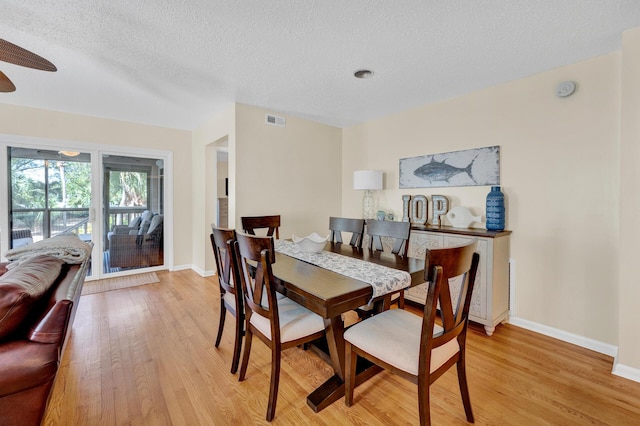 dining space featuring light wood finished floors, baseboards, visible vents, and a textured ceiling