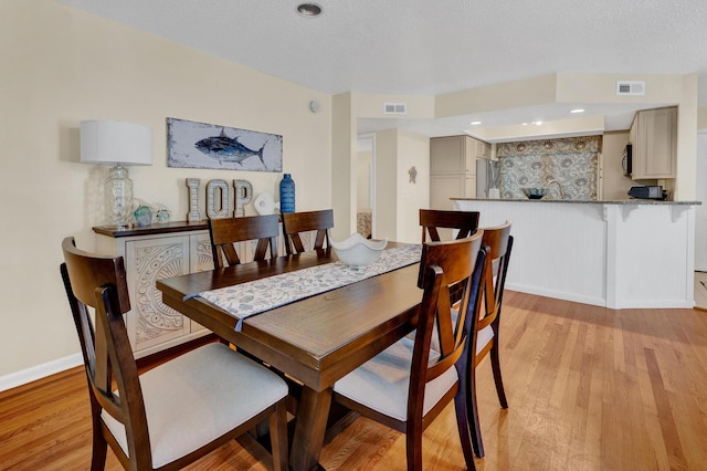 dining space with a textured ceiling, light wood-style flooring, and visible vents