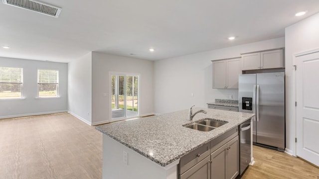 kitchen featuring a kitchen island with sink, sink, light hardwood / wood-style flooring, light stone counters, and stainless steel appliances