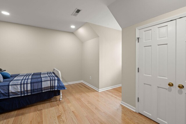 bedroom with light wood-type flooring, vaulted ceiling, and a closet