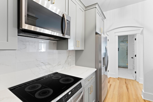 kitchen with light stone countertops, light wood-type flooring, backsplash, stainless steel appliances, and gray cabinets