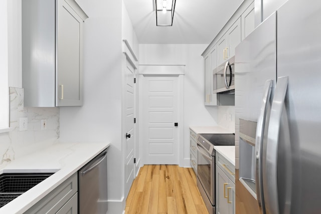 kitchen with gray cabinets, light stone counters, stainless steel appliances, and light hardwood / wood-style floors