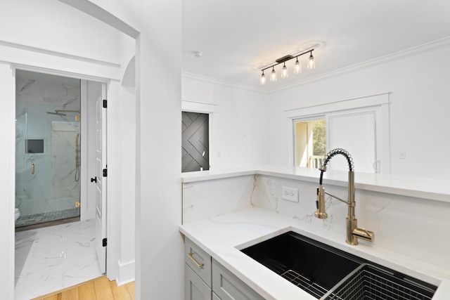 kitchen with light stone countertops, light wood-type flooring, crown molding, and sink