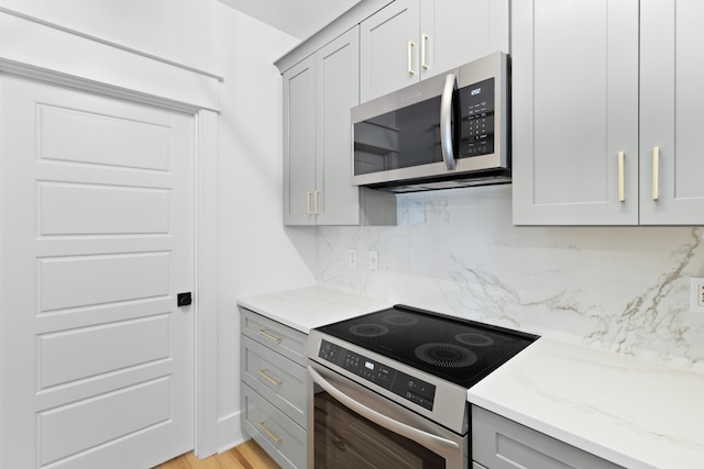 kitchen with gray cabinetry, light stone countertops, tasteful backsplash, light hardwood / wood-style floors, and appliances with stainless steel finishes