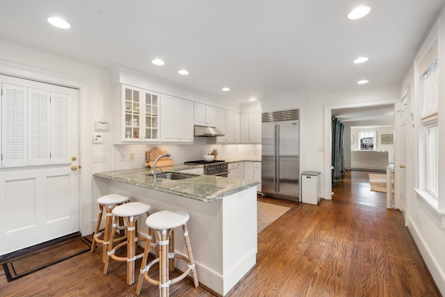 kitchen with sink, high quality appliances, kitchen peninsula, light stone countertops, and white cabinets