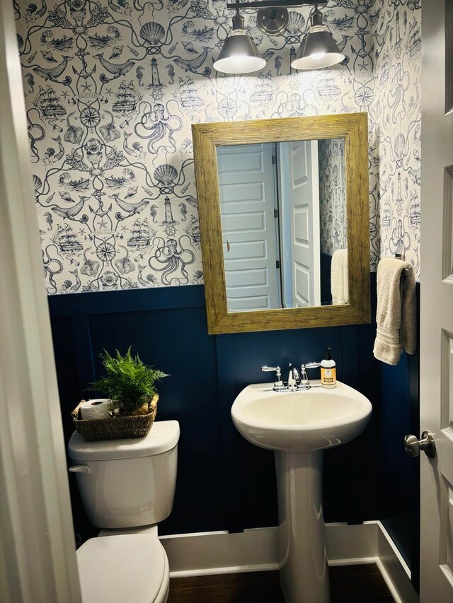 bathroom with toilet, wallpapered walls, and baseboards