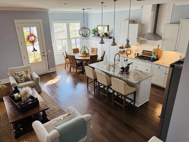 kitchen featuring a kitchen breakfast bar, white cabinetry, stainless steel appliances, wall chimney exhaust hood, and decorative backsplash