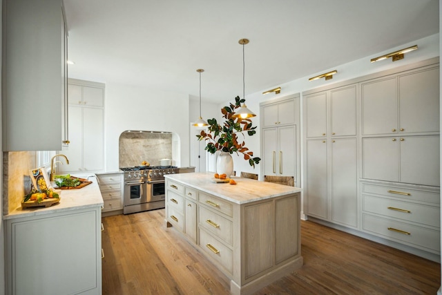 kitchen with double oven range, light wood-type flooring, decorative light fixtures, a kitchen island, and light stone counters