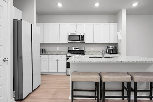 kitchen featuring stainless steel appliances, light wood-style floors, white cabinets, a sink, and a kitchen bar