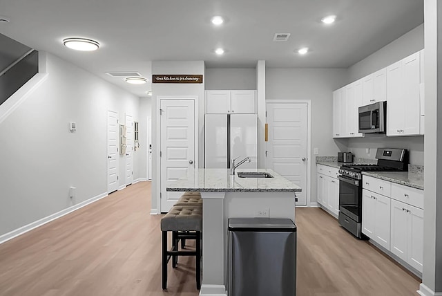 kitchen with light wood finished floors, a breakfast bar area, stainless steel appliances, visible vents, and a sink