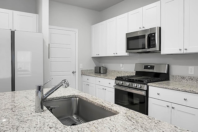 kitchen featuring appliances with stainless steel finishes, white cabinetry, a sink, and light stone countertops