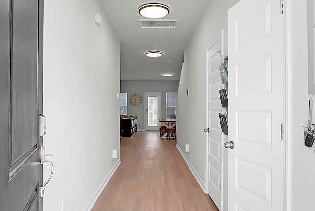 hall with visible vents, light wood-style flooring, and baseboards