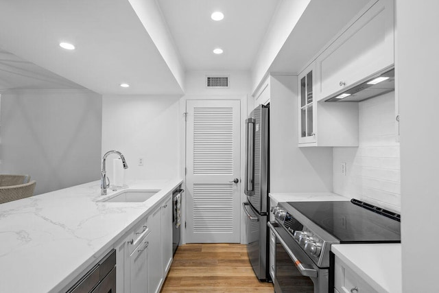 kitchen featuring appliances with stainless steel finishes, light stone counters, sink, light hardwood / wood-style flooring, and white cabinetry