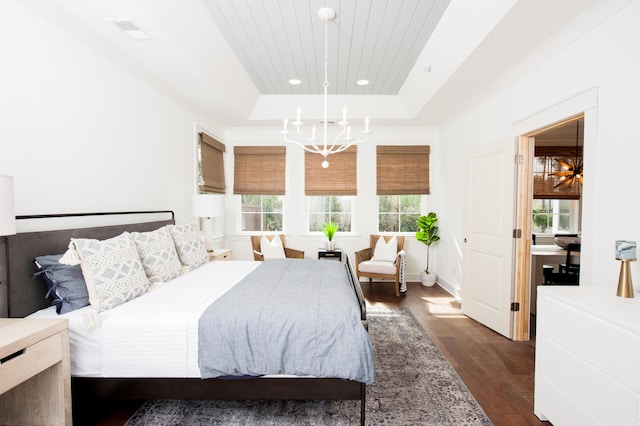 bedroom with a tray ceiling, dark wood-type flooring, visible vents, and an inviting chandelier