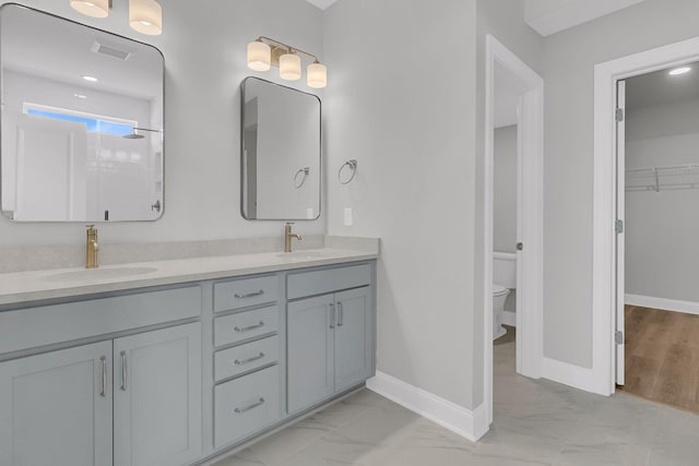 bathroom featuring marble finish floor, double vanity, a sink, and toilet