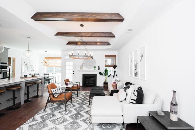 living room featuring beam ceiling, dark wood-style flooring, a notable chandelier, visible vents, and a glass covered fireplace