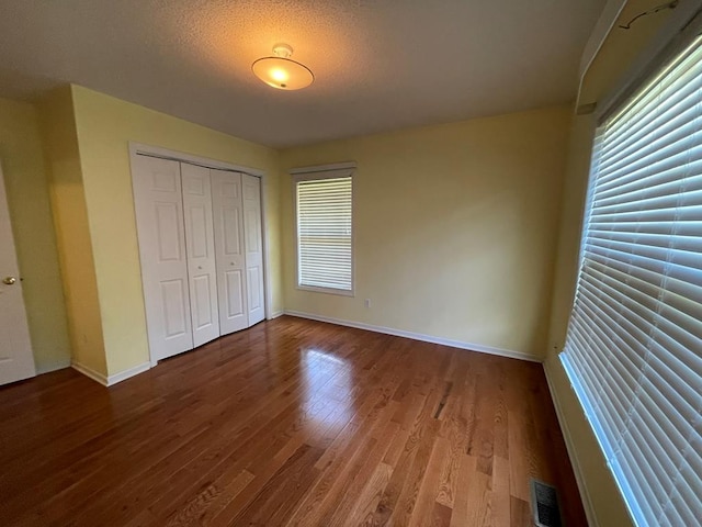 unfurnished bedroom with hardwood / wood-style floors, multiple windows, a closet, and a textured ceiling