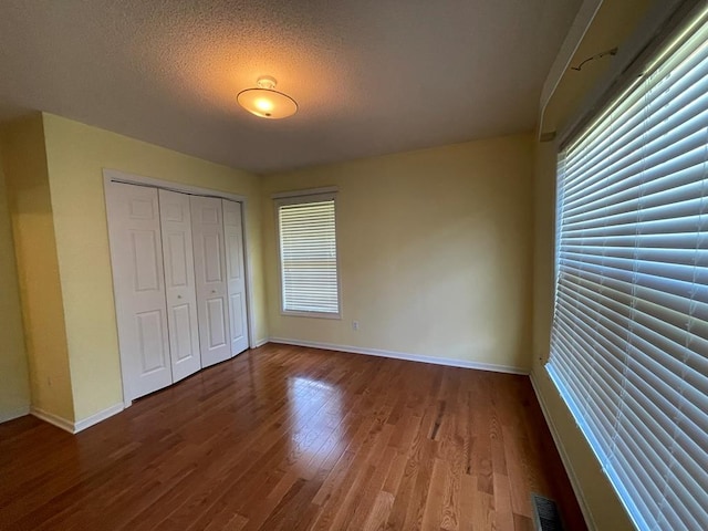 unfurnished bedroom featuring wood-type flooring, a closet, multiple windows, and a textured ceiling