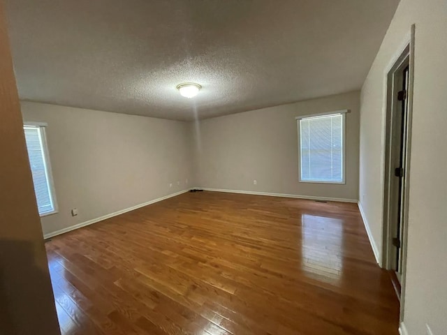 empty room with a textured ceiling, a healthy amount of sunlight, and dark hardwood / wood-style flooring