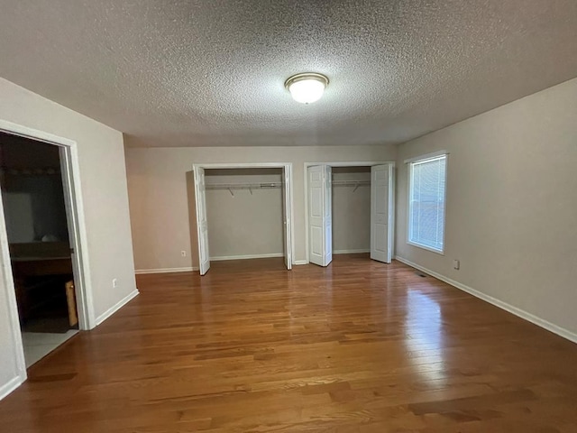 unfurnished bedroom with two closets, hardwood / wood-style floors, and a textured ceiling