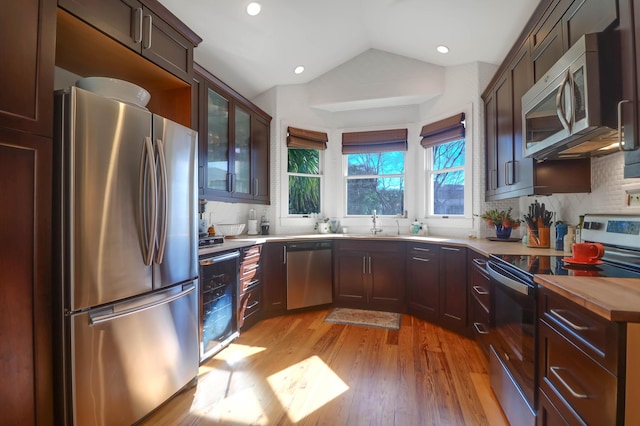 kitchen featuring beverage cooler, backsplash, lofted ceiling, appliances with stainless steel finishes, and light wood-type flooring