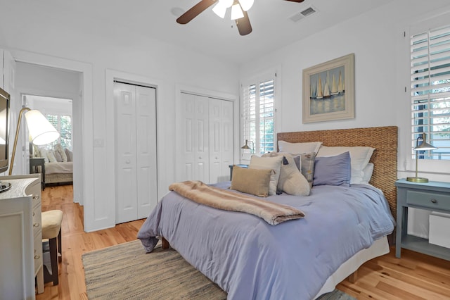 bedroom with light wood-type flooring, ceiling fan, and multiple closets