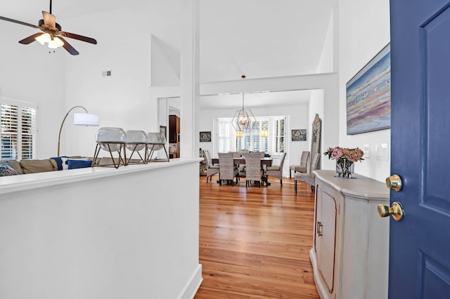 entryway featuring light hardwood / wood-style flooring, a towering ceiling, and ceiling fan with notable chandelier