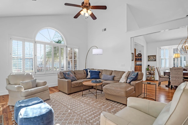 living room with ceiling fan with notable chandelier, high vaulted ceiling, and light hardwood / wood-style flooring