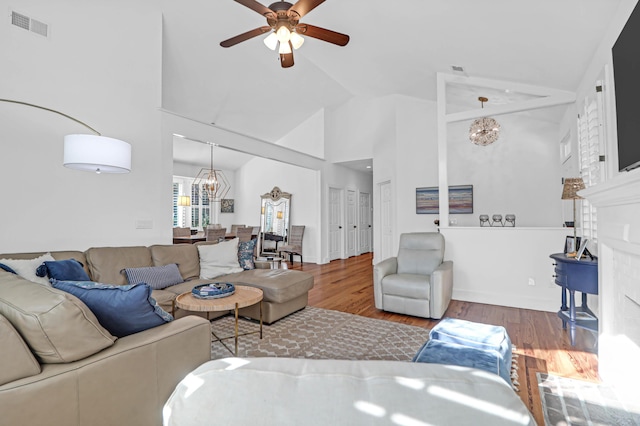 living room with hardwood / wood-style floors, ceiling fan with notable chandelier, and high vaulted ceiling