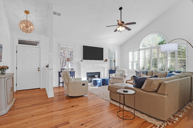 living room with a fireplace, high vaulted ceiling, ceiling fan with notable chandelier, and light wood-type flooring