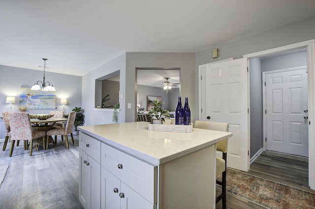 kitchen featuring dark wood-type flooring, hanging light fixtures, a breakfast bar area, ceiling fan with notable chandelier, and white cabinets