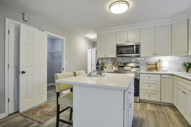 kitchen with a breakfast bar area, appliances with stainless steel finishes, light wood-type flooring, a center island, and white cabinets