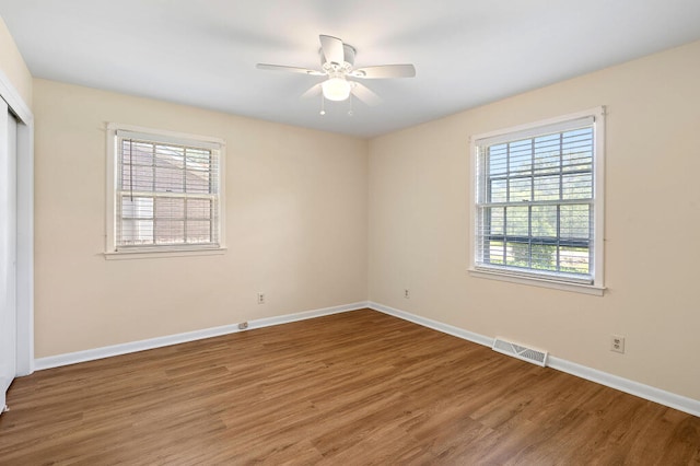 unfurnished room featuring visible vents, plenty of natural light, baseboards, and wood finished floors