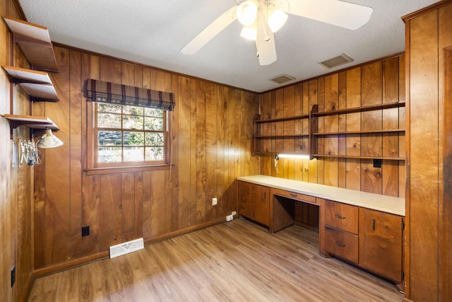 unfurnished office with light wood-type flooring, visible vents, a ceiling fan, and built in desk