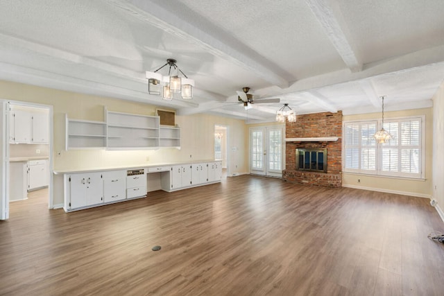 unfurnished living room with ceiling fan with notable chandelier, beamed ceiling, wood finished floors, and a textured ceiling