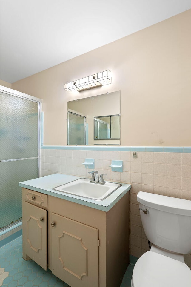 bathroom with a wainscoted wall, toilet, tile walls, a shower stall, and vanity