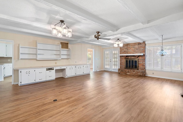 unfurnished living room with beamed ceiling, ceiling fan with notable chandelier, light wood-type flooring, and a textured ceiling