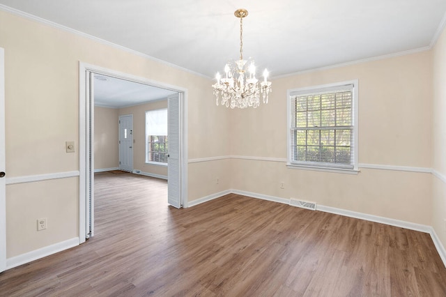 spare room featuring a chandelier, ornamental molding, baseboards, and wood finished floors