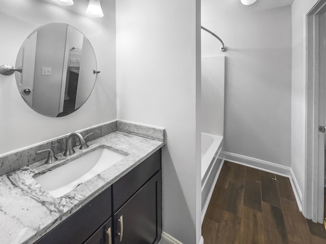bathroom with wood finished floors, vanity, baseboards, and washtub / shower combination