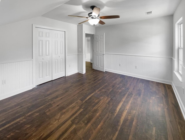 unfurnished bedroom with dark wood finished floors, wainscoting, a ceiling fan, vaulted ceiling, and a closet