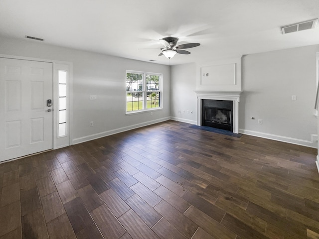 unfurnished living room featuring ceiling fan, dark wood finished floors, baseboards, and a fireplace with flush hearth